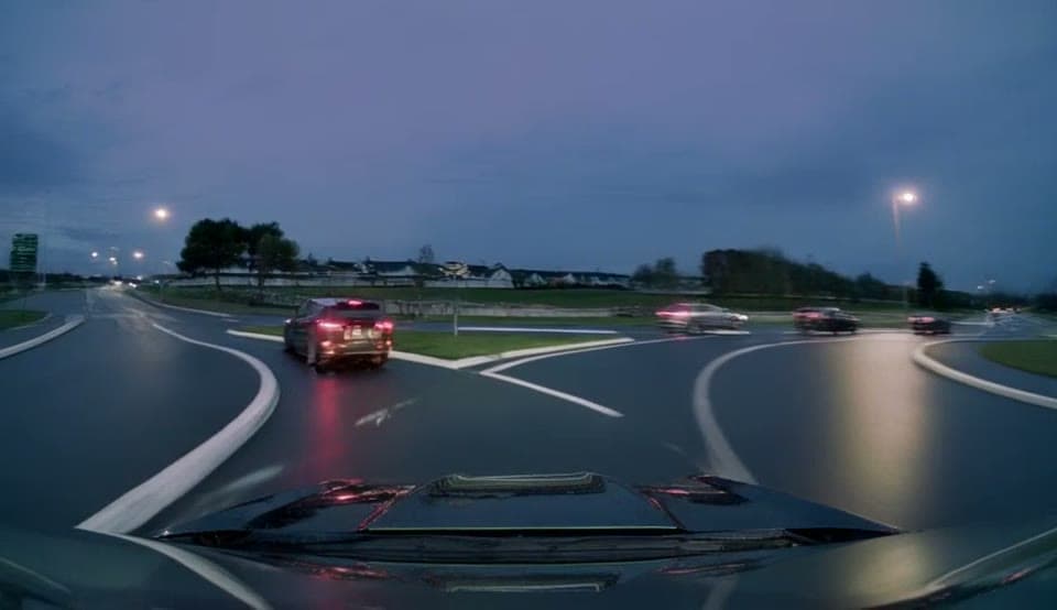 A dashcam-style frame of the roundabout in rain at dusk, generated by the model, not a photograph.