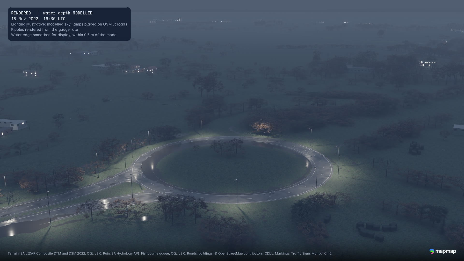 A roundabout on the bypass at 16:30 UTC in the last of the daylight, lamps coming on, trees and fields around it.